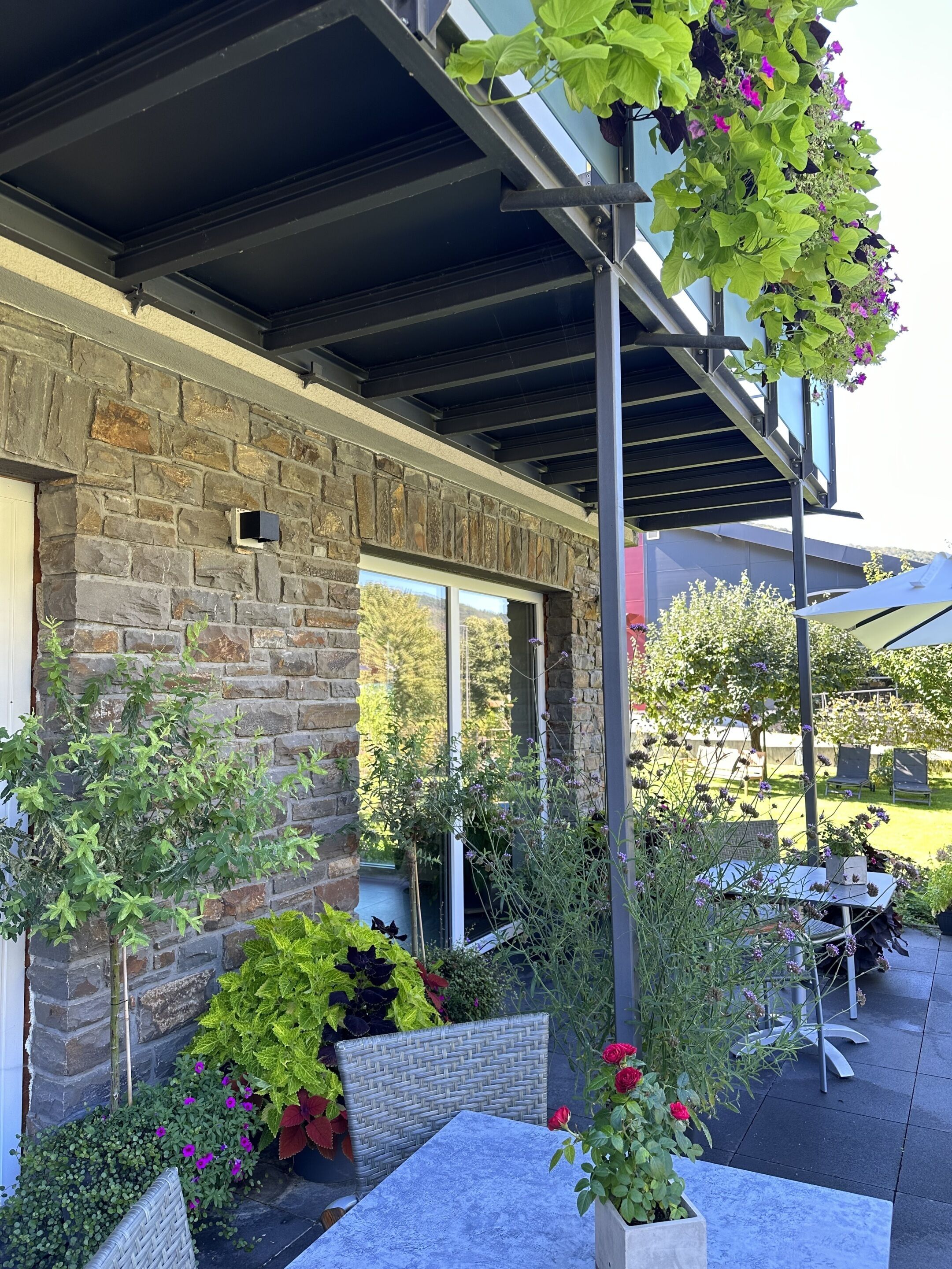 Ein Steingebäude mit überdachter Terrasse, Sitzgelegenheiten und Kübelpflanzen.
