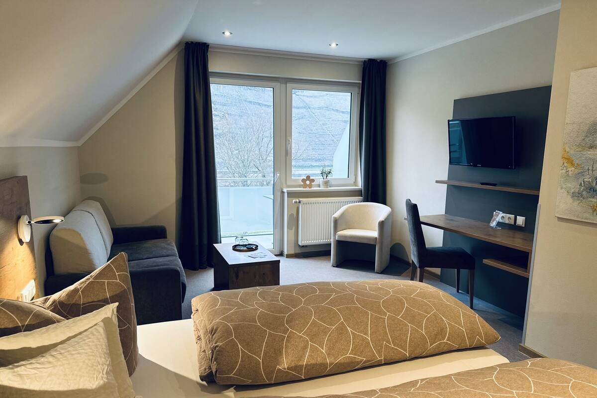 A hotel room with a bed, a desk, a chair, a TV, and a window with curtains.