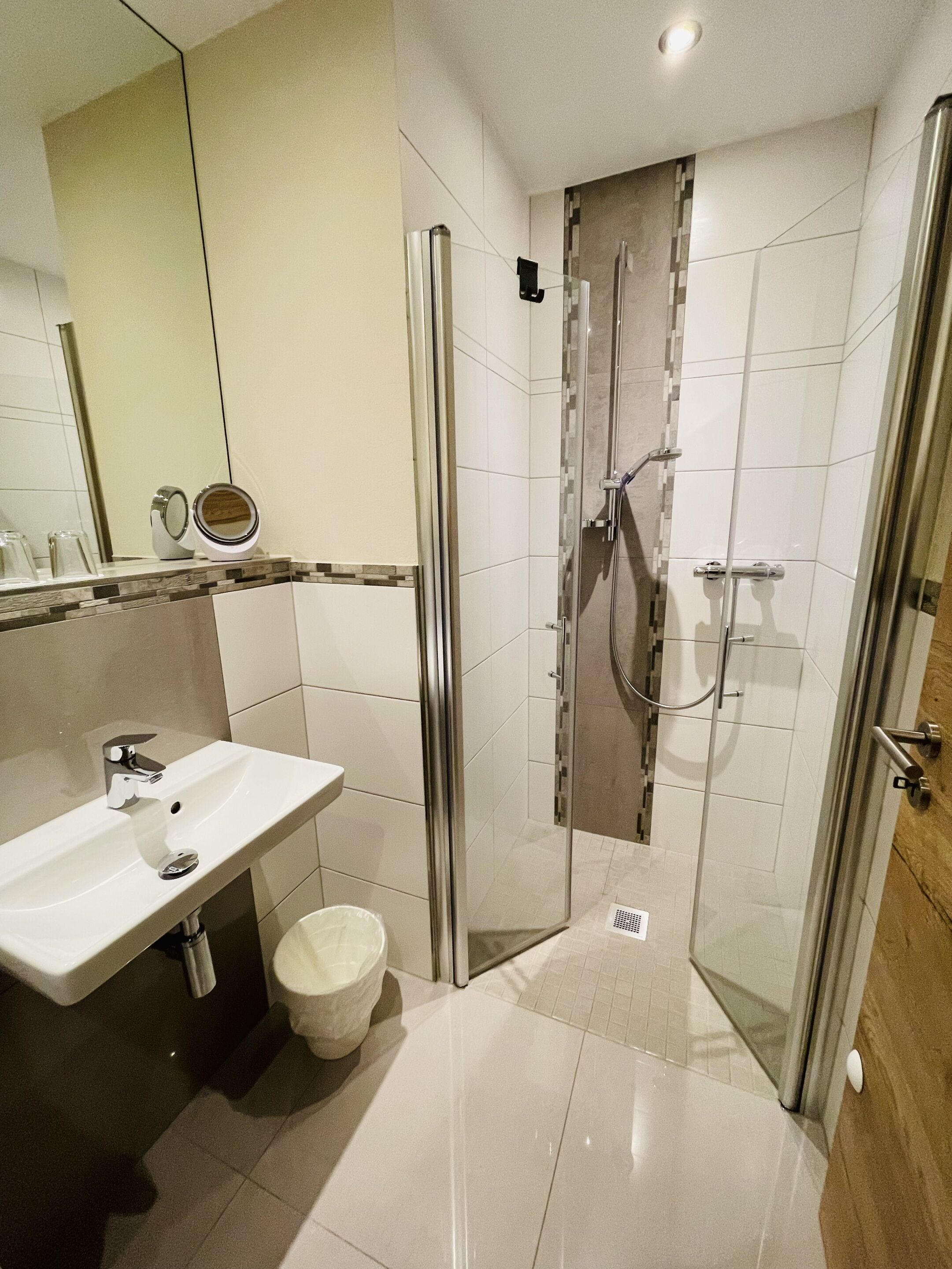 Ein modernes Badezimmer mit einer gläsernen Duschkabine, einem weißen Waschbecken und einem Spiegel.