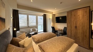 Habitación de hotel con cama, escritorio, silla, televisor y armario.