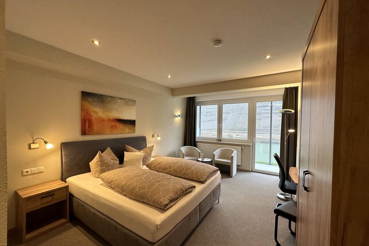 A modern hotel room with a large bed, bedside tables, a desk, and a chair.