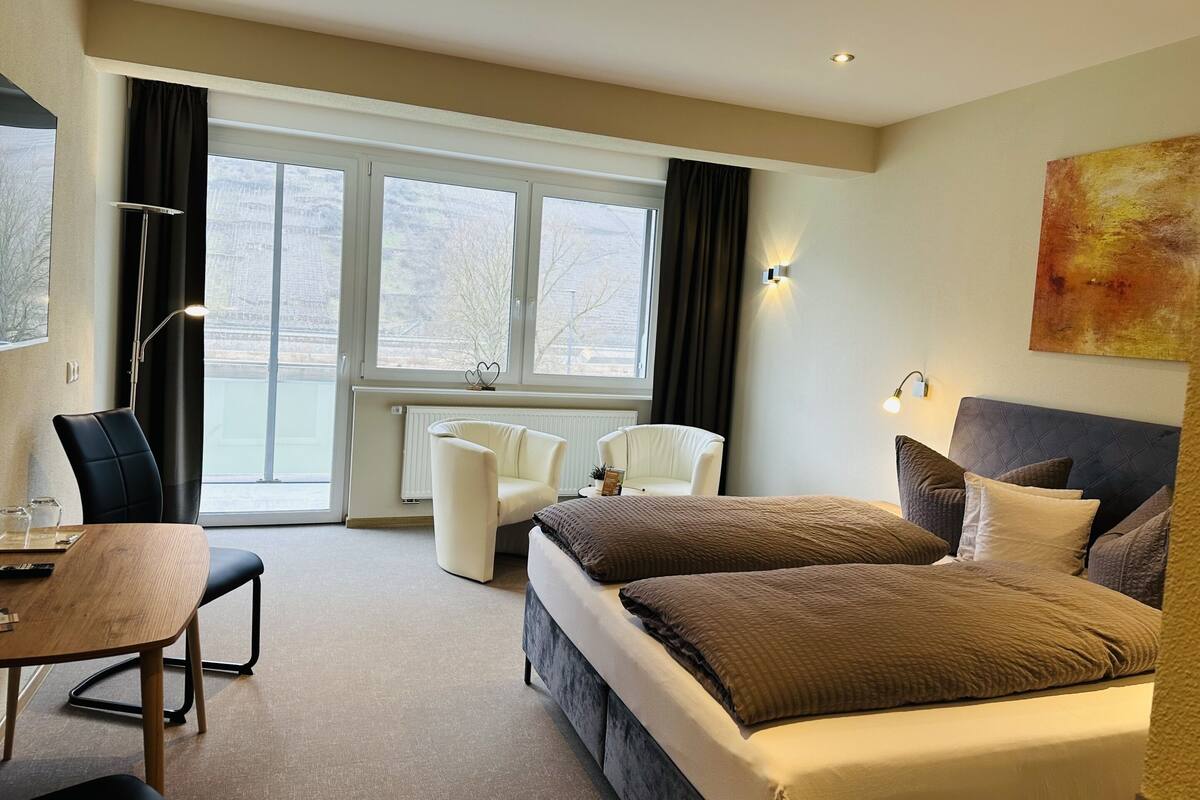 A hotel room with a bed, two chairs, a desk, and a large window.