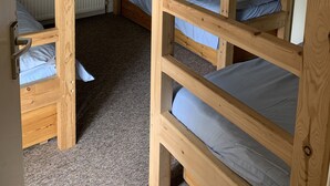 Quarto com beliche, escada de madeira, radiador e chão coberto de carpete.