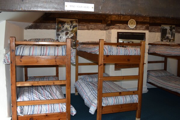 Camas literas con ropa de cama a rayas en una habitación rústica con vigas de madera a la vista y un reloj en la pared.