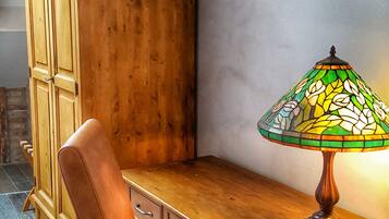 A wooden desk with a stained glass lamp, a leather chair, and a wooden cabinet in a room with sloped ceilings and a tiled floor.