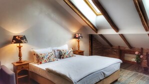 A bedroom with a large bed, two bedside tables with lamps, a skylight, wooden beams, and a brick wall. - Windmill Studios (Bucharest)