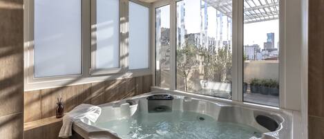Un baño moderno con una bañera grande, paredes de madera y vistas a la ciudad a través de amplios ventanales.
