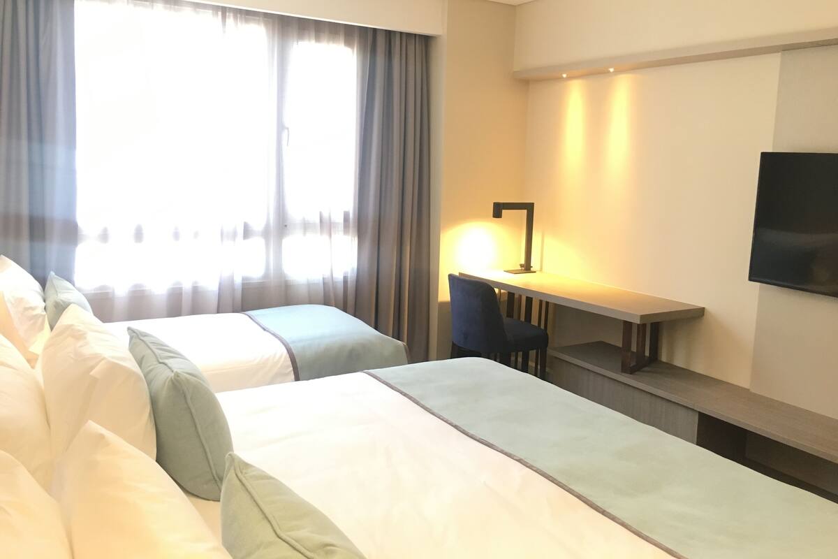 A hotel room with two beds, a desk, a chair, and a TV.