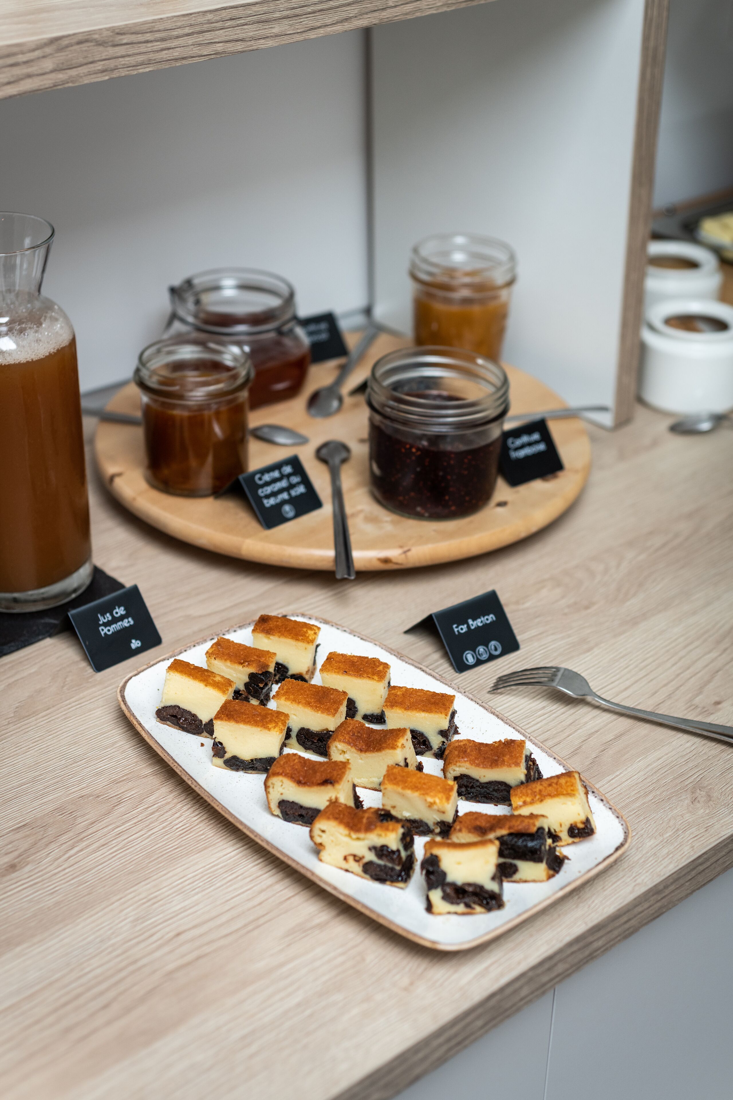 A dessert display with various sweets and jars of jam on a wooden board.
