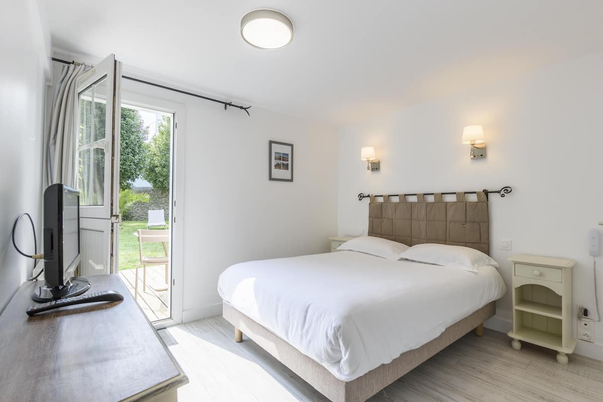 A bedroom with a bed, bedside tables, a TV, and a window with curtains.