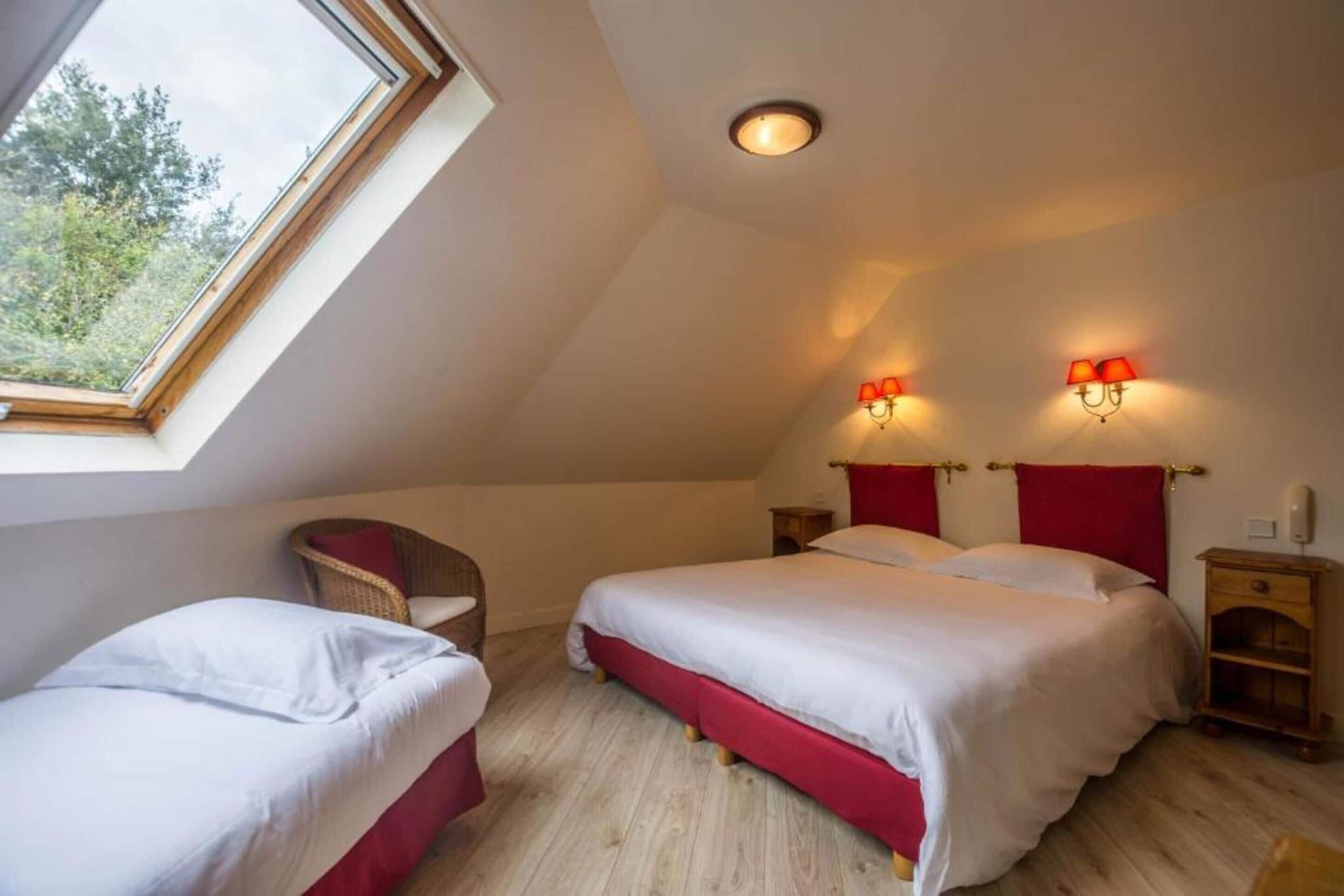 Een slaapkamer met twee bedden, een dakraam en een rode accentmuur.