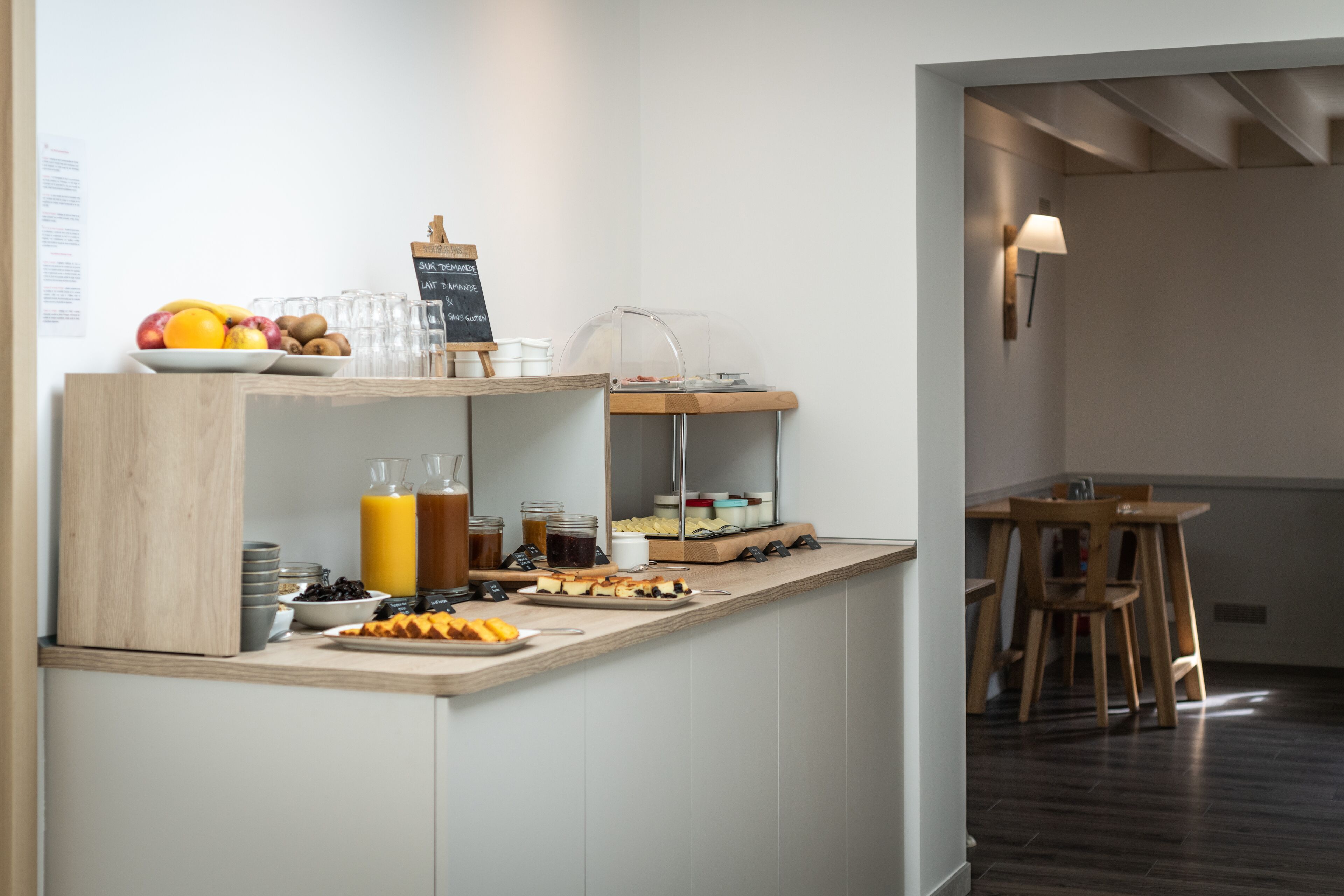 A breakfast bar with a variety of food items and beverages, a chalkboard menu, and a seating area with a table and chairs.