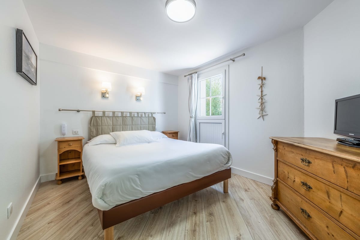 A bedroom with a bed, wooden nightstand, dresser, and a television.