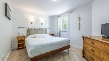 Un dormitorio con cama, mesita de noche de madera, cómoda y televisor.