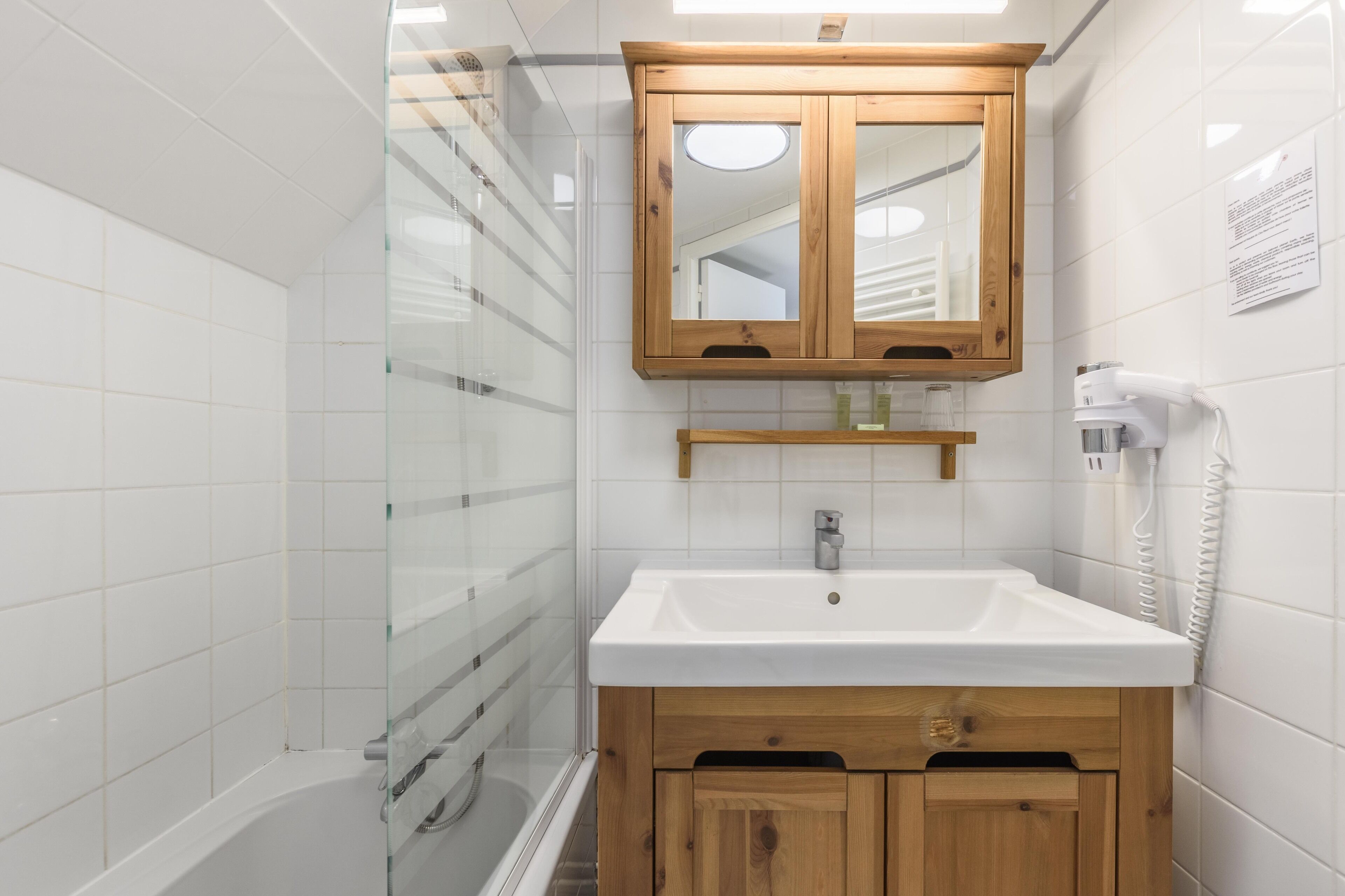 A bathroom with a white sink, wooden cabinets, a glass shower enclosure, and a mounted mirror.