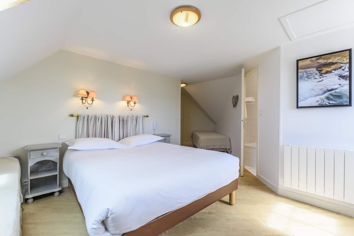A bedroom with a large bed, bedside lamps, a nightstand, and a view of the sea through an open door.