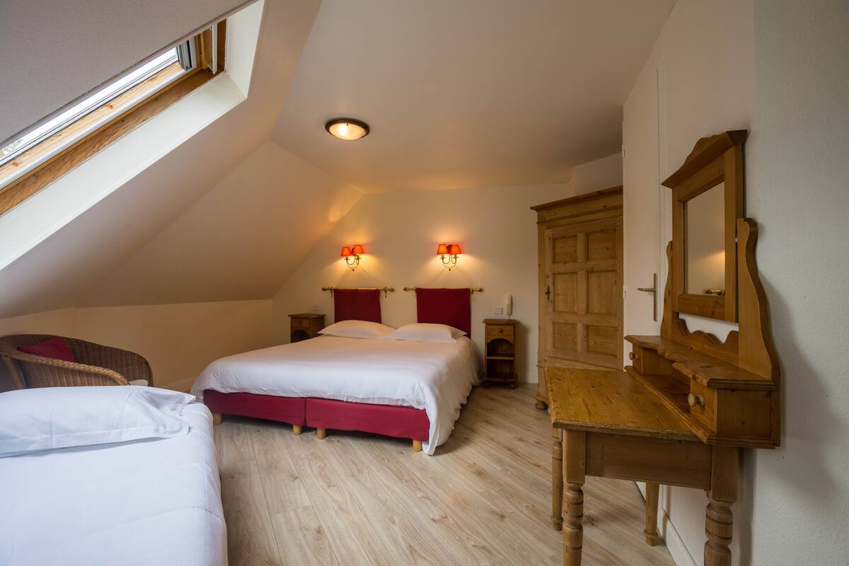 A bedroom with a sloped ceiling, two beds, a wooden dresser, and a mirror.