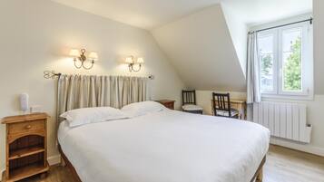 Een slaapkamer met een groot bed, twee nachtkastjes, een stoel, een raam met gordijnen en wandlampen.