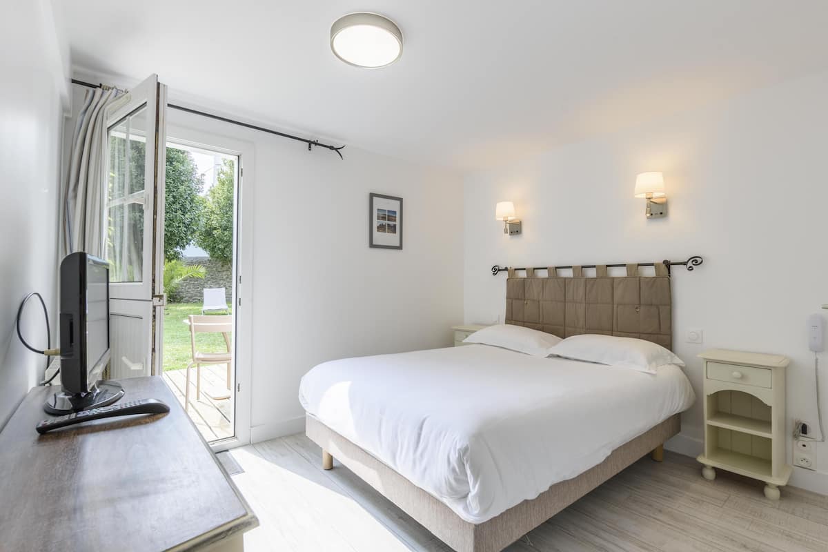 A bedroom with a bed, bedside tables, a desk with a computer, and a window with curtains.