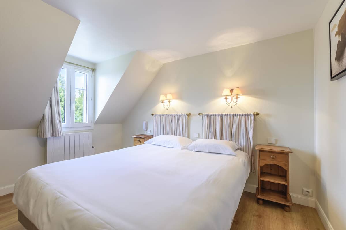 A bedroom with a large bed, two bedside tables, a window, and a sloped ceiling.