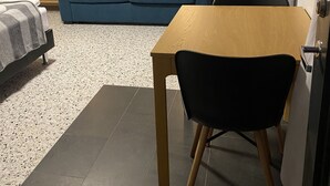 A room with a blue sofa, a wooden table, a black chair, a TV, and a bookshelf with books. - Sólheimar Studio Apartments (Isafjordur)