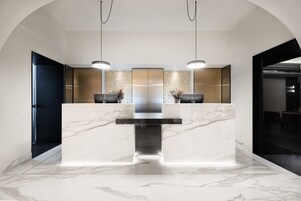 Uma área de recepção moderna com balcão de mármore, duas luminárias pendentes e uma parede decorativa.