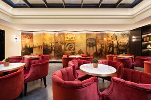 Un restaurante con mesas redondas y sillas de terciopelo rojo, que presenta un gran mural con diversas escenas.