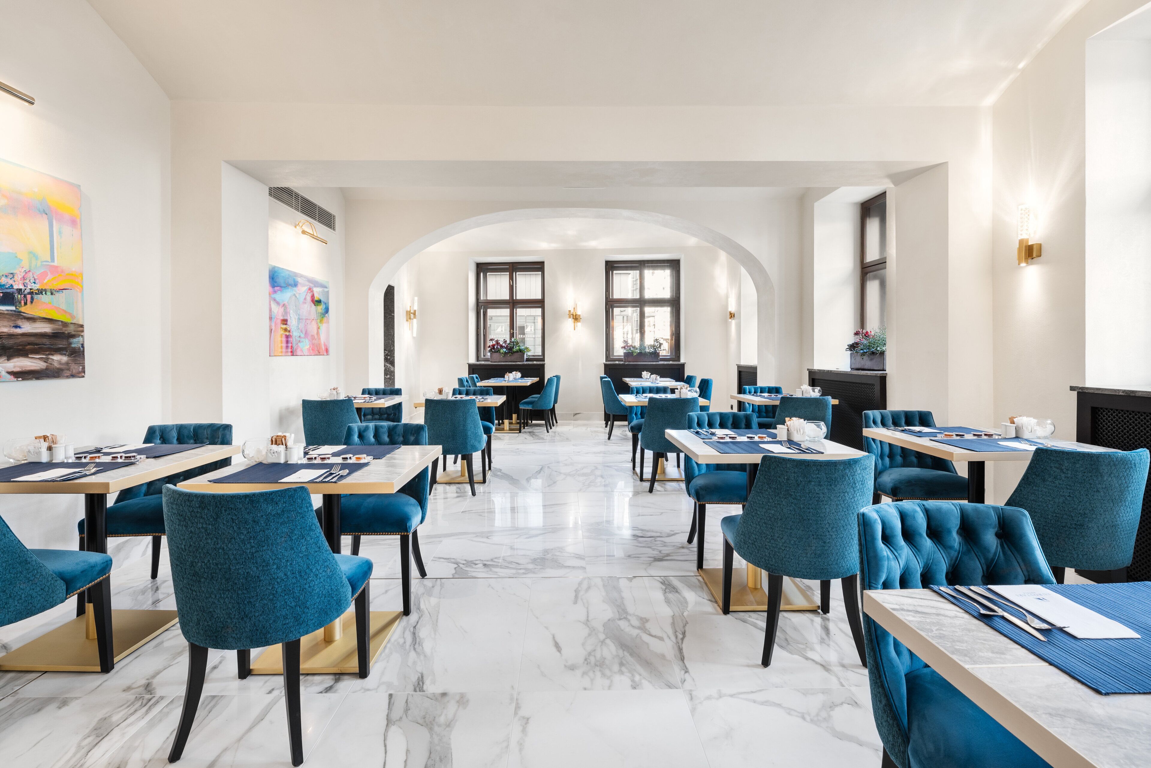 A modern dining area with marble flooring, blue upholstered chairs, and tables arranged in a spacious layout.
