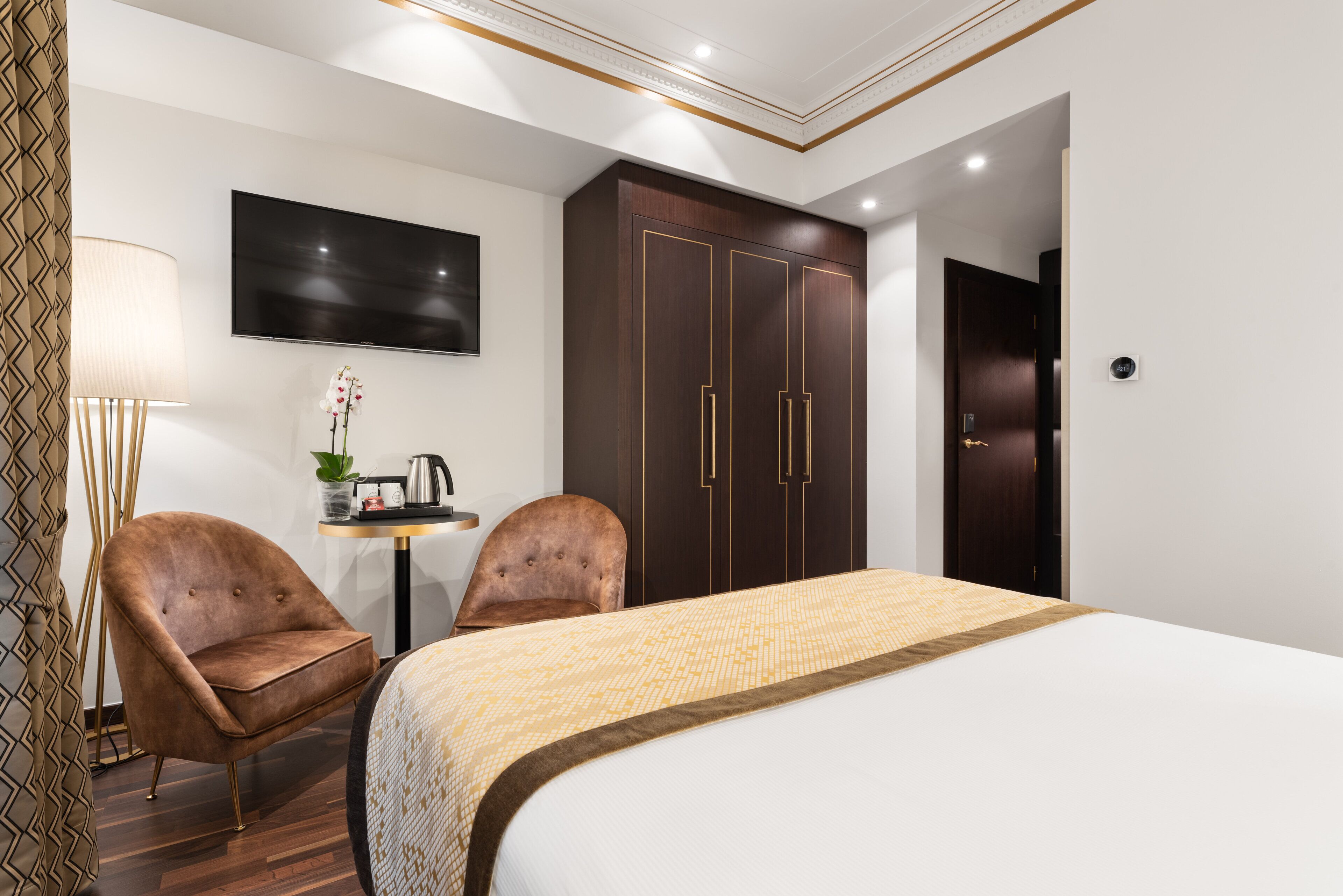 A hotel room with a bed, two armchairs, a desk with a lamp, a TV, and a wardrobe.