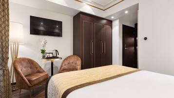 A hotel room with a bed, two armchairs, a desk with a lamp, a TV, and a wardrobe.