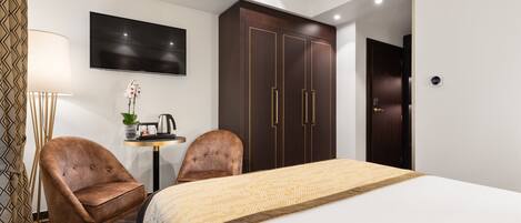 A hotel room with a bed, two armchairs, a desk with a lamp, a TV, and a wardrobe.