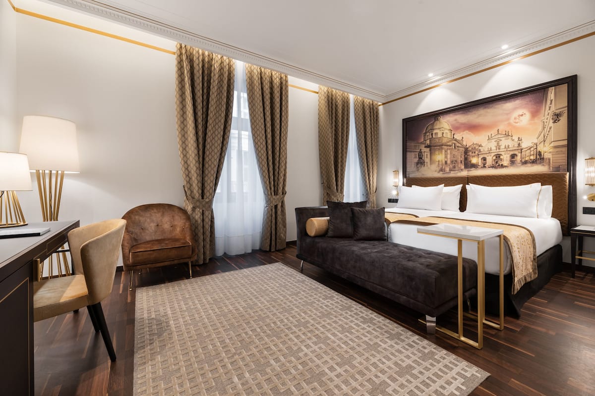A hotel room with a bed, a desk, a chair, and a large painting on the wall.