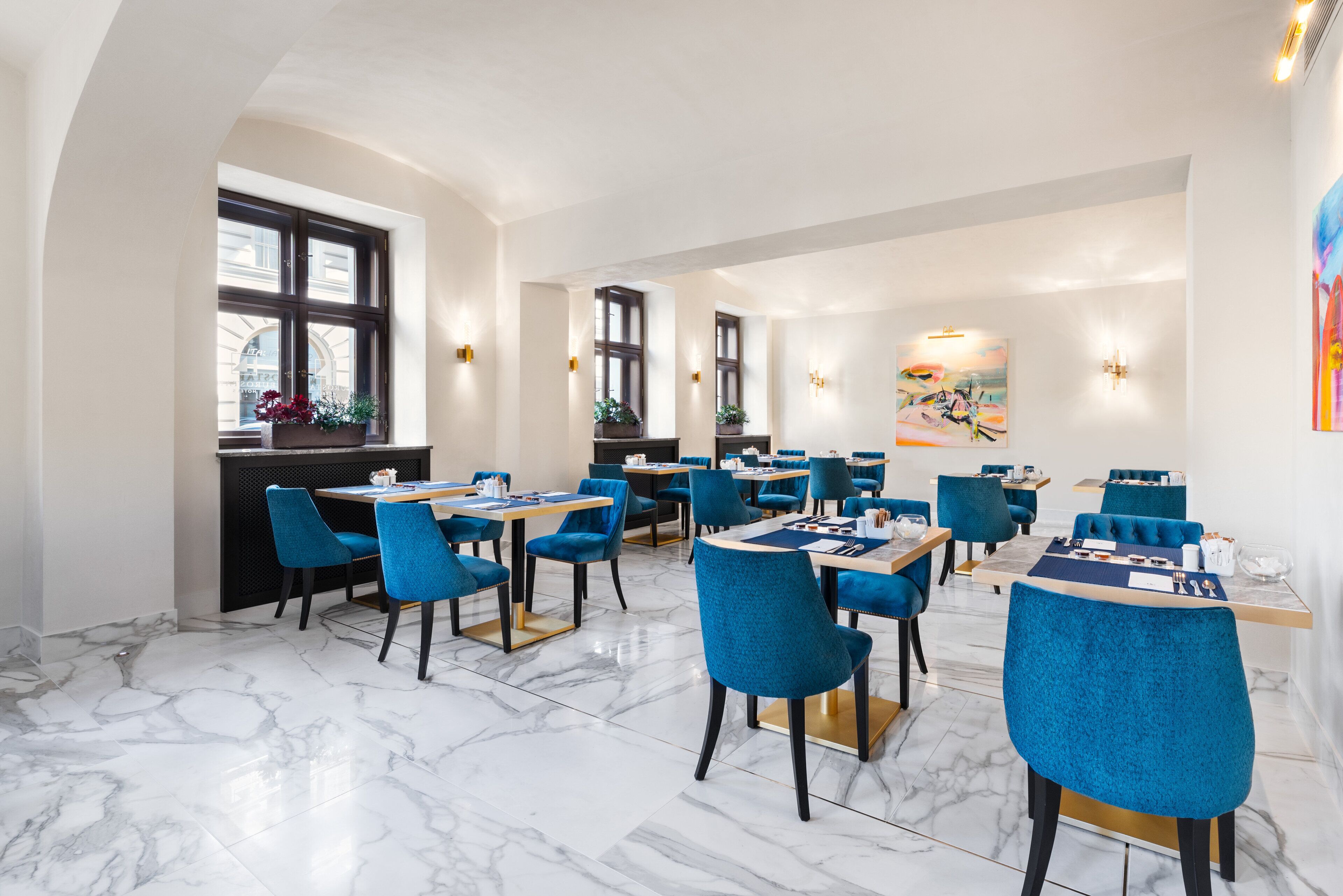 A modern dining area with marble flooring, blue upholstered chairs, and tables set for dining.