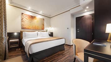 Una habitación de hotel con una cama grande, un escritorio, una silla, un cuadro en la pared y una puerta.
