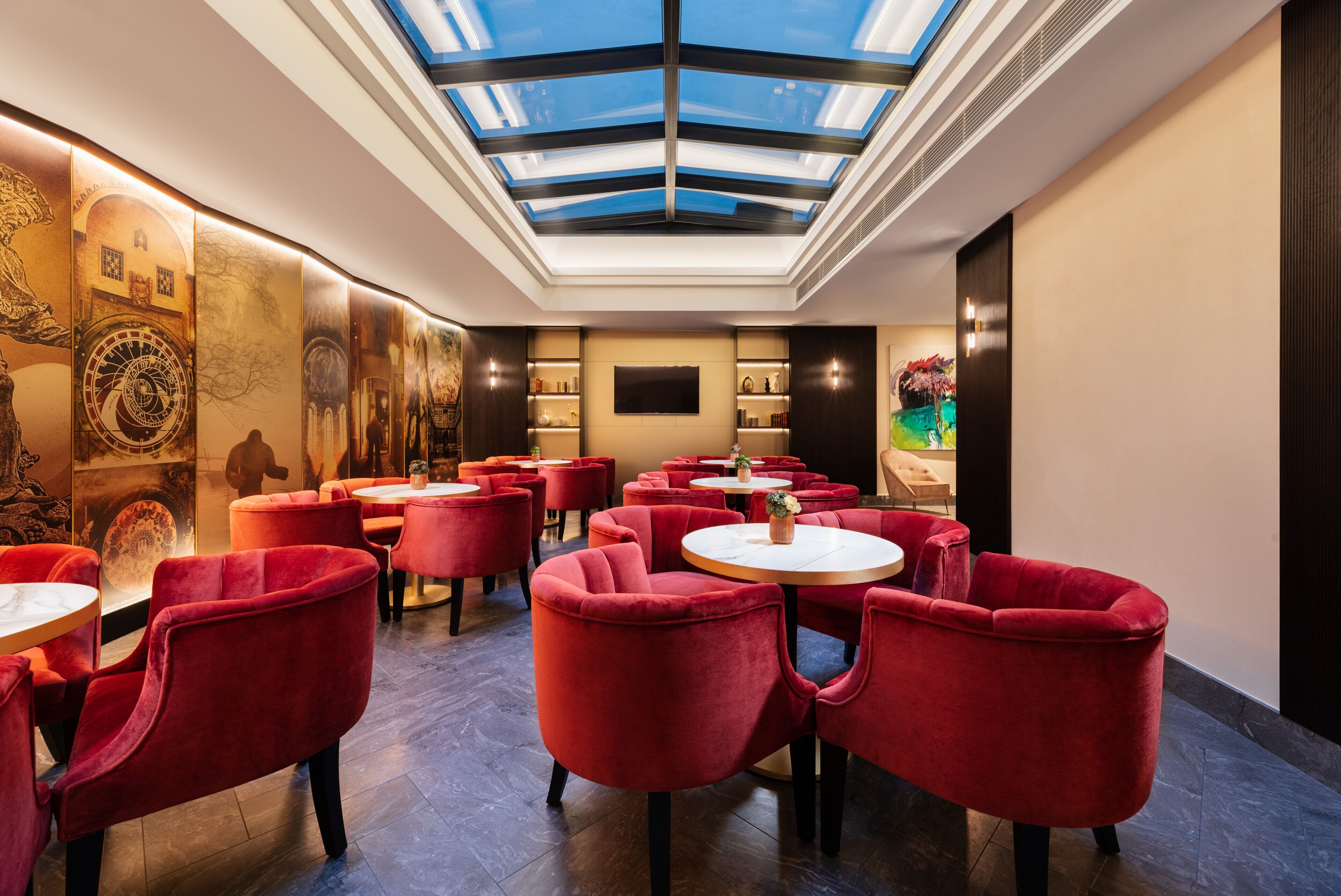 A modern interior with a skylight, red velvet chairs, and a central table.