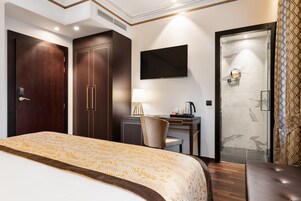 Quarto de hotel com uma cama grande, uma escrivaninha com cadeira, uma TV na parede e área de chuveiro.