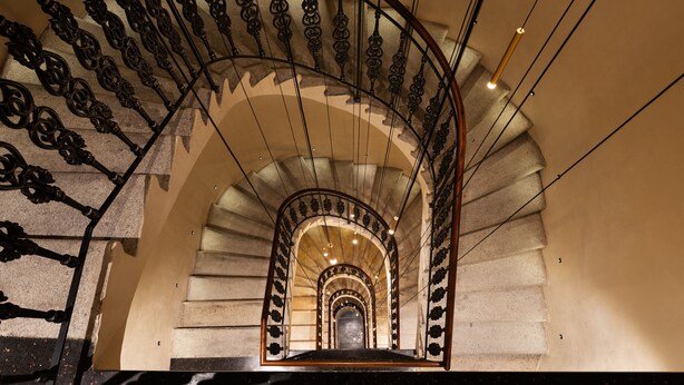 Un escalier en colimaçon avec des rampes en métal ouvragé et un mur en pierre.