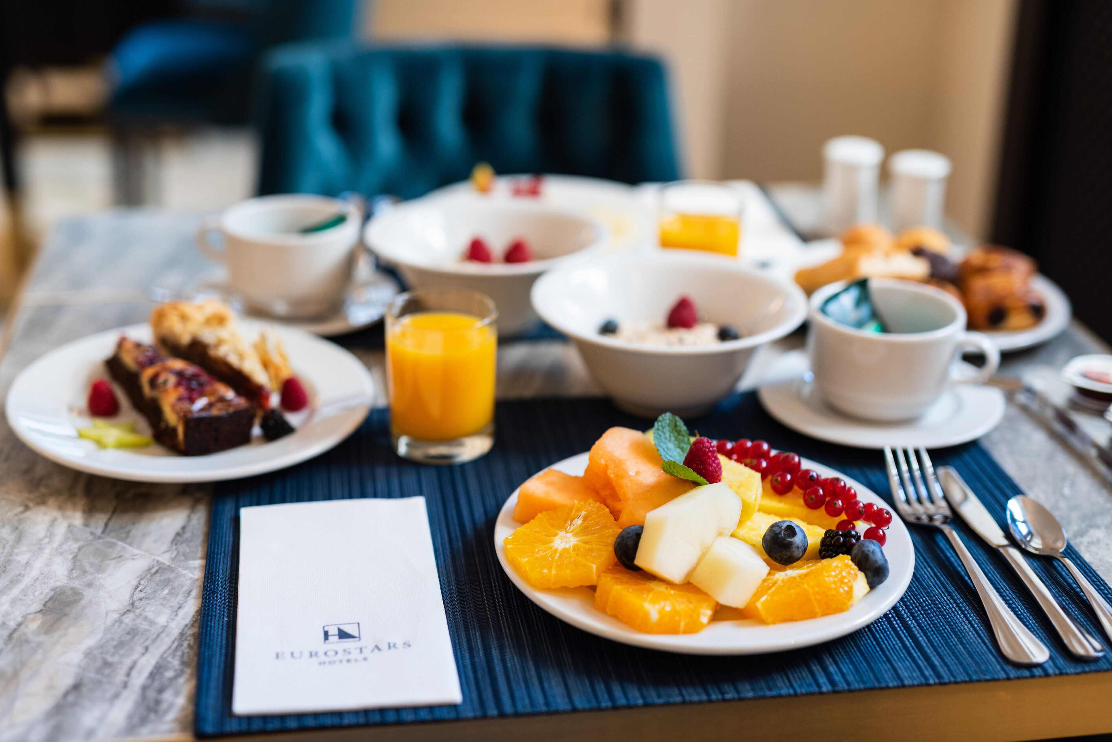 A breakfast setting with plates of fruit, pastries, and a coffee cup on a table.