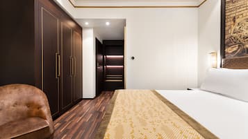 A hotel room with a large bed, a brown leather chair, dark wooden wardrobes, and a wall-mounted lamp.
