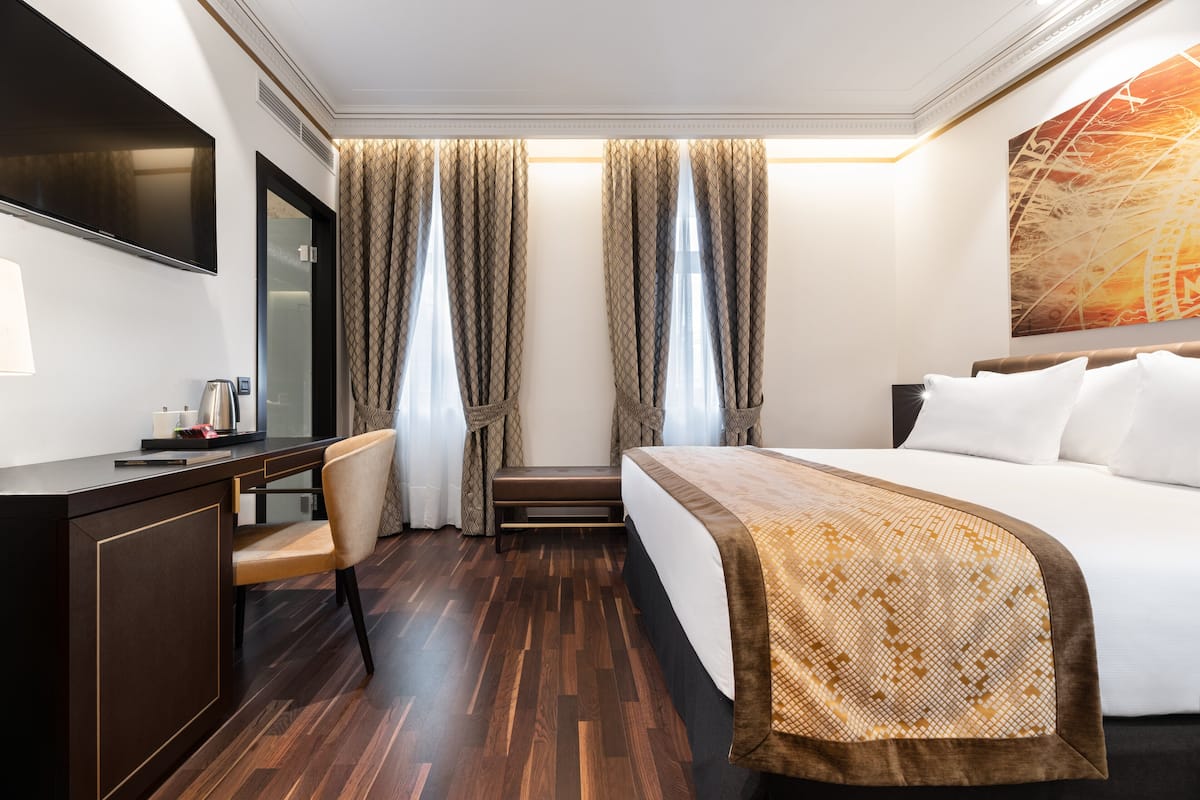 A hotel room with a bed, a desk, a chair, a TV, and curtains.