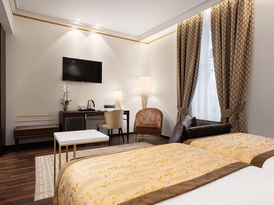 A hotel room with two beds, a desk, a chair, a TV, and a window with curtains.