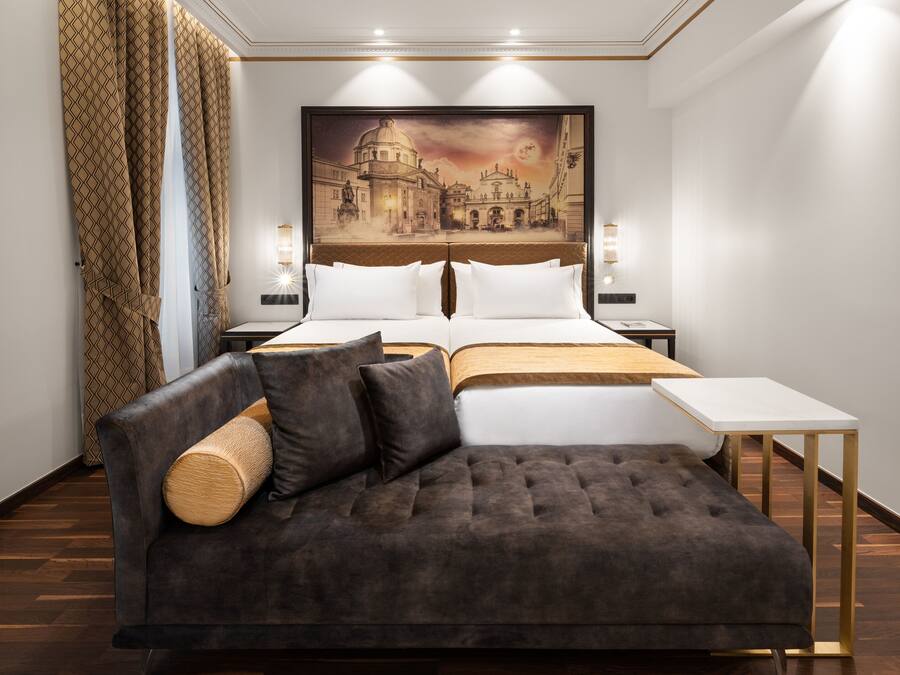 Un hotel moderno con una cama grande, un sofá, una mesita y un cuadro de un paisaje urbano en la pared.