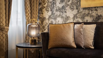 A dark-colored sofa with patterned cushions, a round side table with a lamp, and a patterned wall behind.