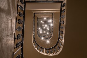 Uma escadaria em espiral com guarda-corpos de metal ricamente decorados e uma série de luzes no topo.