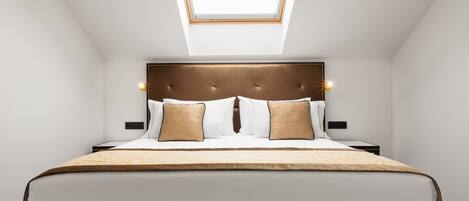 Une chambre avec une lucarne, une tête de lit capitonnée et un lit avec une literie blanche et deux oreillers.