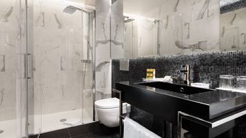 Un baño moderno con cabina de ducha de vidrio, tocador con lavamanos negro y un inodoro blanco.