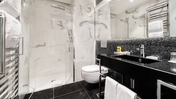 Een moderne badkamer met een douche met glazen wand, een zwart marmeren wastafelmeubel en een wit toilet.