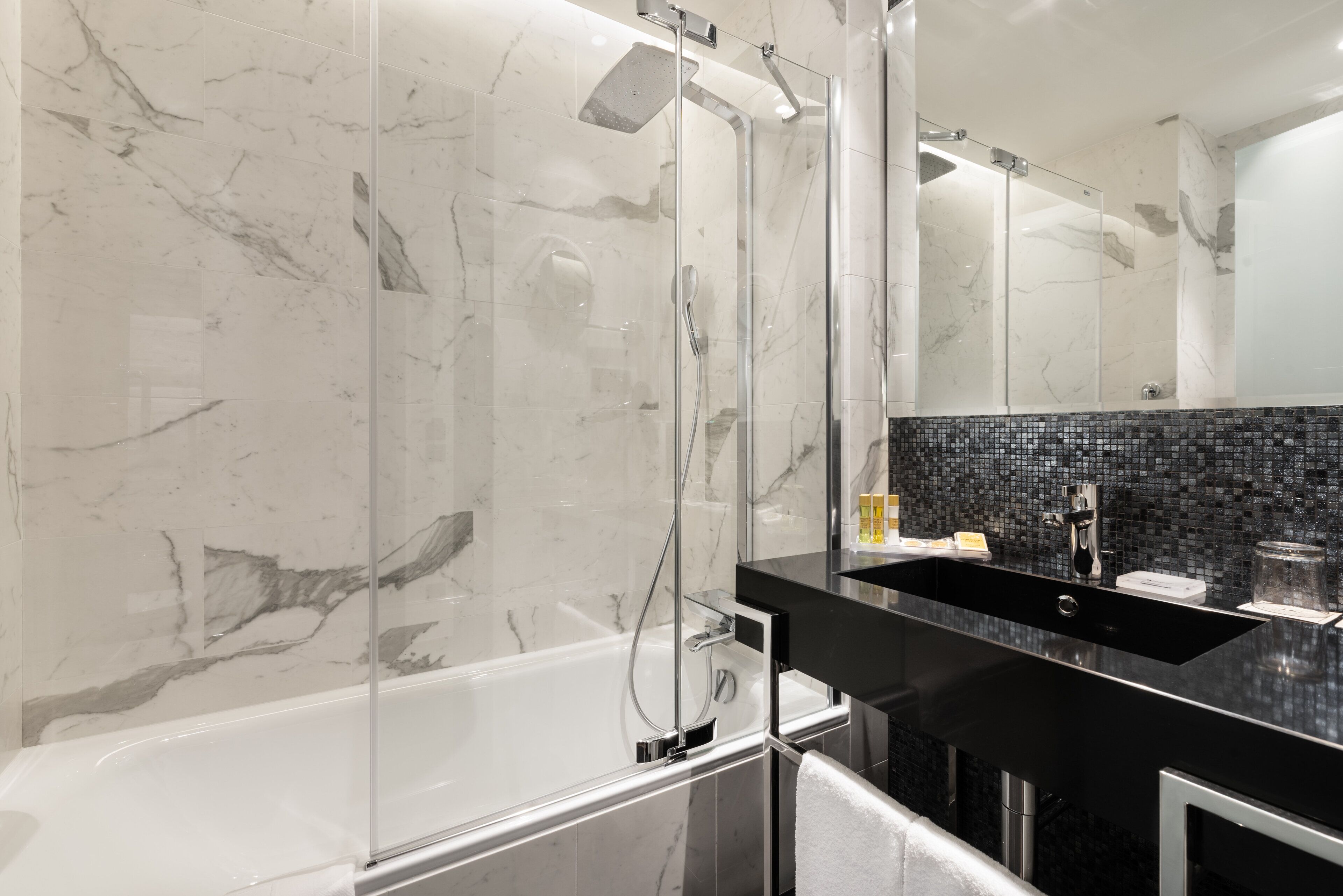 Un baño moderno con ducha envuelta en vidrio, lavamanos de superficie negra e impermeable de azulejos.