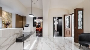 Un hall d’entrée moderne avec un comptoir de réception en marbre, un espace salon avec des fauteuils orange et un canapé en cuir noir.