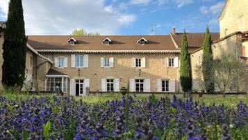 A stone building with multiple windows and a garden with purple flowers in front.